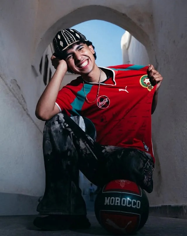 Smiling Morocco supporter holding a signed red football shirt beneath an arch