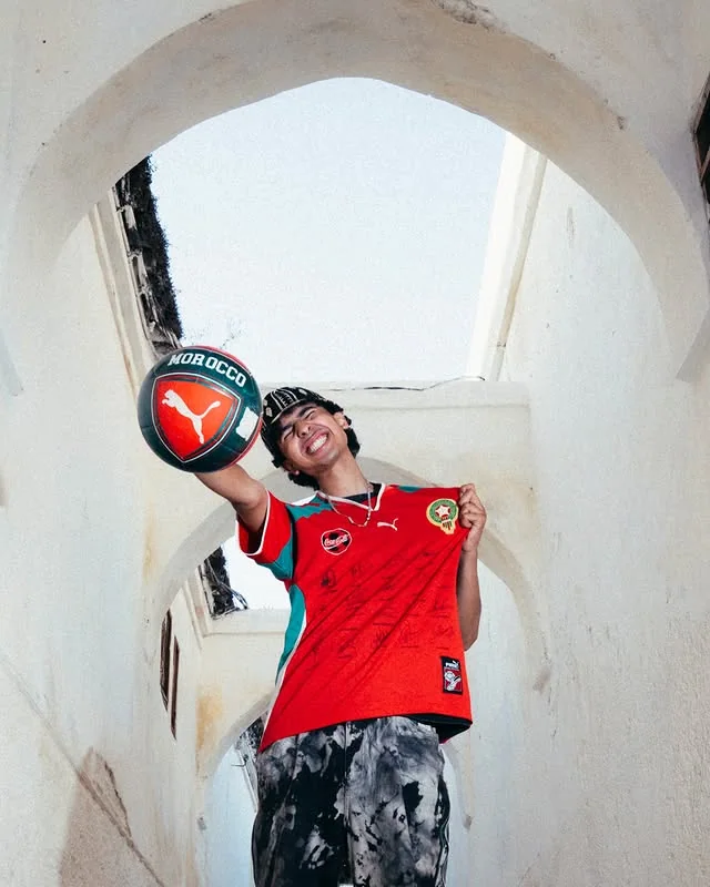 Smiling supporter presenting a football beneath white medina arches